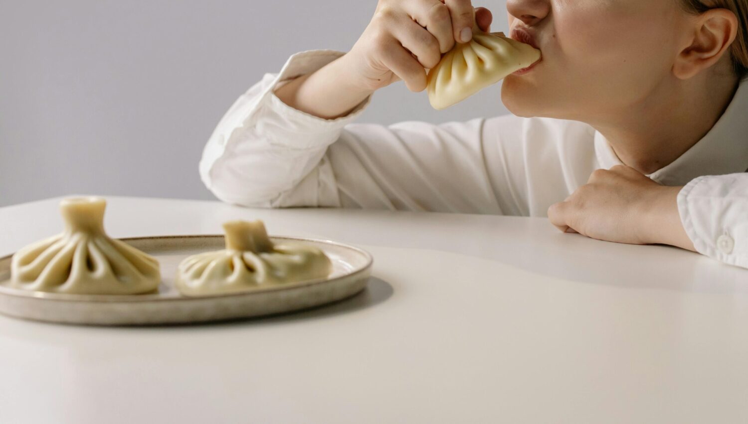 Young woman savoring traditional Georgian khinkali dumplings indoors at lunch.